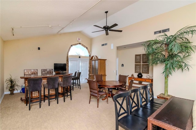 dining area featuring ceiling fan, light colored carpet, rail lighting, and vaulted ceiling