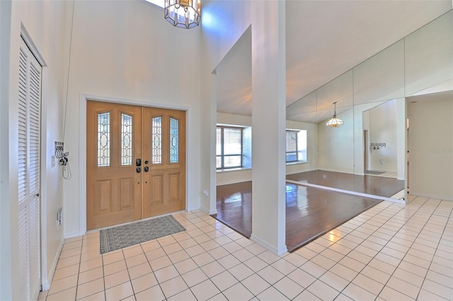 foyer featuring light tile patterned flooring, high vaulted ceiling, and a chandelier