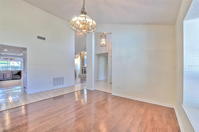 spare room featuring light hardwood / wood-style floors, a chandelier, and a high ceiling