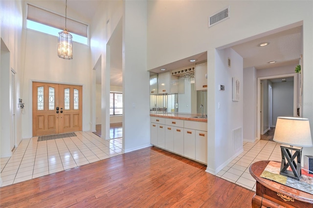 foyer entrance featuring a towering ceiling, sink, a chandelier, and light hardwood / wood-style flooring