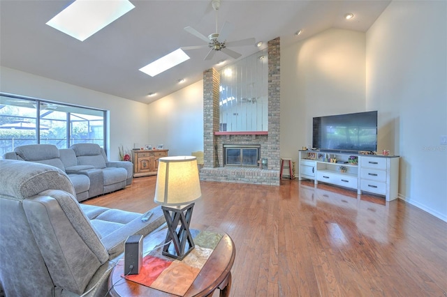 living room with a fireplace, hardwood / wood-style flooring, a skylight, and high vaulted ceiling