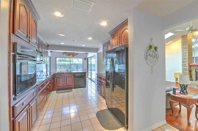 kitchen featuring a brick fireplace, light tile patterned floors, a textured ceiling, ceiling fan, and black appliances