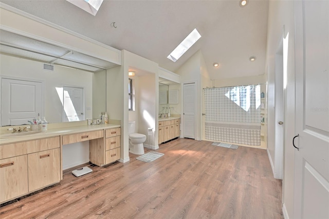 bathroom with vaulted ceiling with skylight, a bathtub, hardwood / wood-style flooring, vanity, and toilet