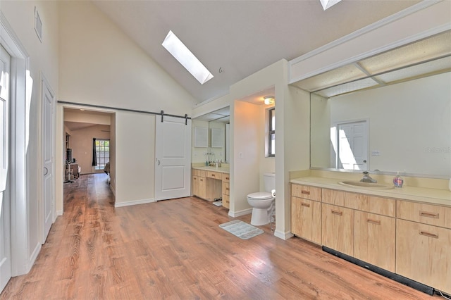 bathroom featuring high vaulted ceiling, a skylight, wood-type flooring, vanity, and toilet