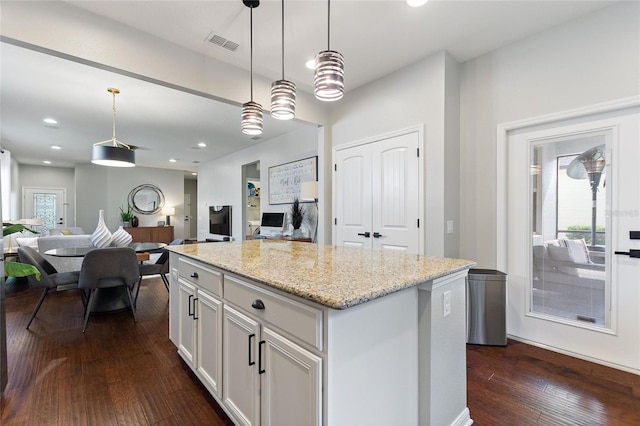 kitchen with pendant lighting, a center island, light stone countertops, and white cabinets