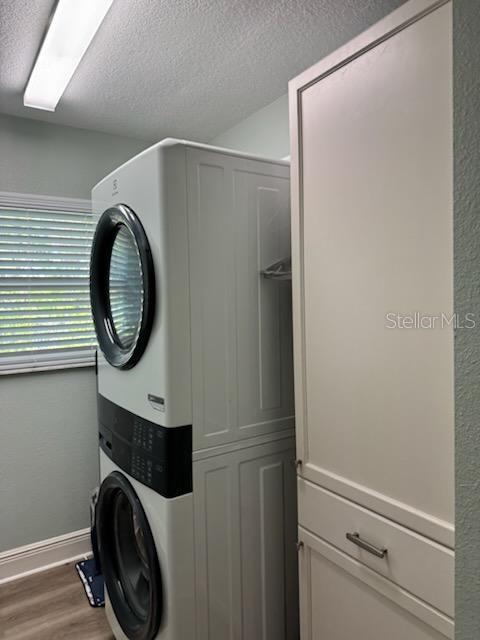 laundry room featuring cabinets, stacked washer / drying machine, hardwood / wood-style floors, and a textured ceiling