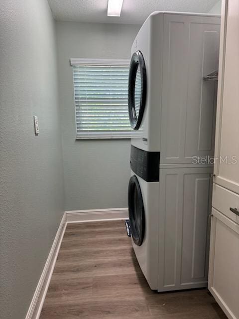 laundry area with stacked washer and dryer, hardwood / wood-style floors, and a textured ceiling