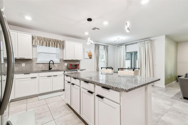 kitchen with white cabinetry, light stone counters, a center island, hanging light fixtures, and stainless steel refrigerator