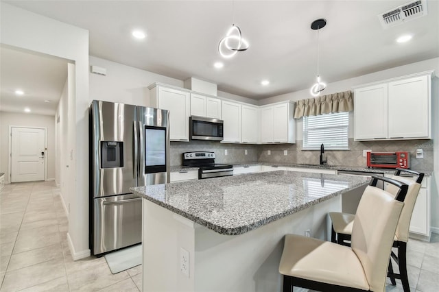 6684 Devlin Ln, Wesley Chapel, FL 33545 - kitchen with stainless steel appliances, backsplash, white cabinetry, visible vents, and a kitchen island