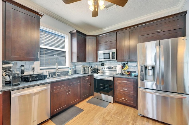 kitchen featuring appliances with stainless steel finishes, sink, light wood-type flooring, and dark stone counters