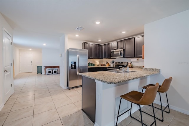 kitchen featuring sink, a breakfast bar, stainless steel appliances, light stone countertops, and kitchen peninsula