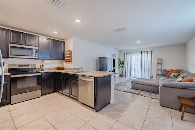 kitchen featuring sink, appliances with stainless steel finishes, light stone counters, light tile patterned flooring, and kitchen peninsula