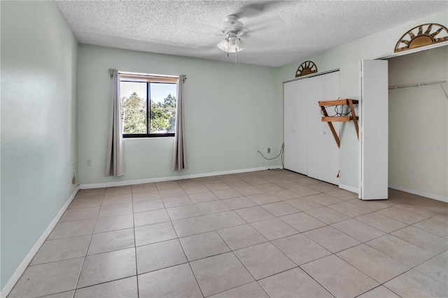 unfurnished bedroom with ceiling fan, light tile patterned flooring, a textured ceiling, and a closet