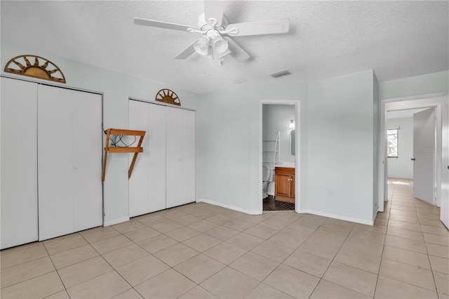 unfurnished bedroom featuring multiple closets, light tile patterned flooring, ceiling fan, and a textured ceiling