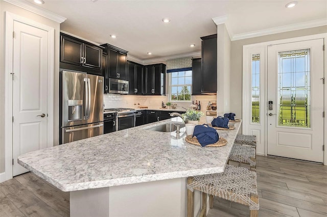 kitchen featuring sink, a breakfast bar area, a kitchen island with sink, stainless steel appliances, and light wood-type flooring