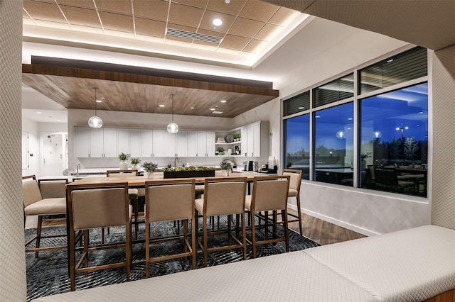 bar featuring hanging light fixtures, wood-type flooring, and white cabinets