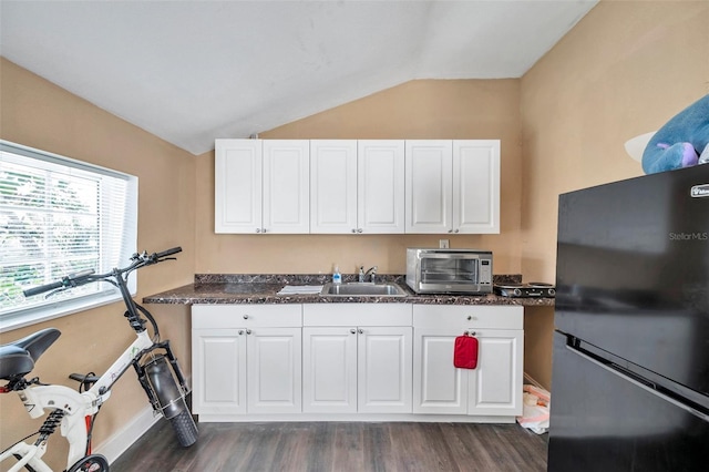 kitchen with sink, vaulted ceiling, white cabinets, and black fridge