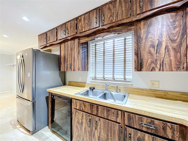 kitchen featuring dark brown cabinetry, sink, light tile patterned floors, stainless steel fridge, and black dishwasher