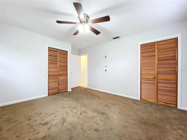 unfurnished bedroom with dark colored carpet, two closets, and ceiling fan