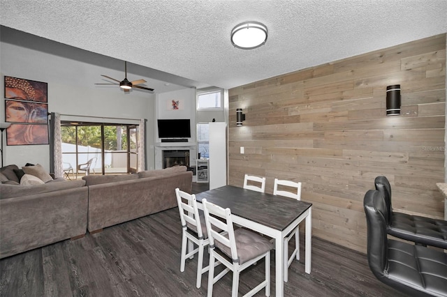 dining space with a fireplace, dark hardwood / wood-style flooring, ceiling fan, a textured ceiling, and wooden walls