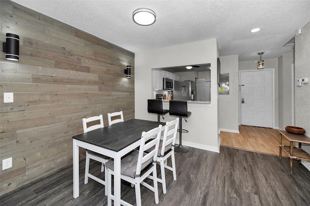 dining space featuring a textured ceiling, wooden walls, and dark hardwood / wood-style floors