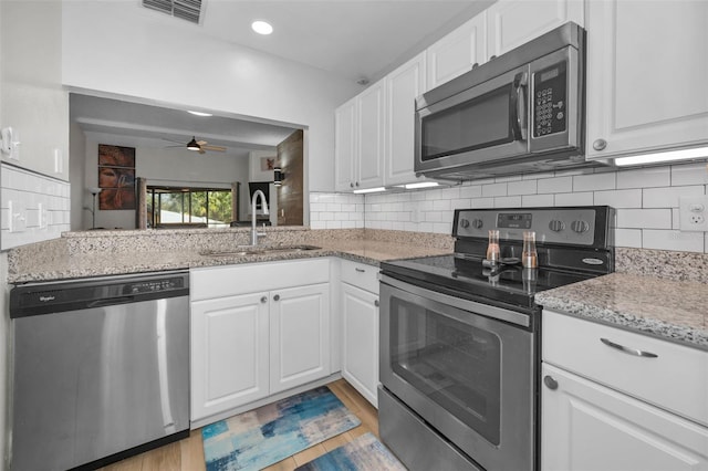 kitchen featuring stainless steel appliances, backsplash, light stone counters, ceiling fan, and white cabinets