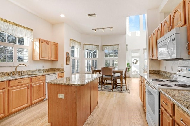 kitchen with a center island, sink, light stone counters, and white appliances