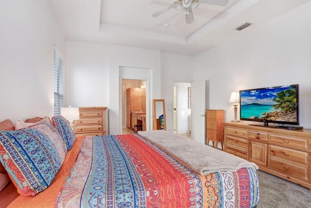 carpeted bedroom featuring ceiling fan, connected bathroom, and a tray ceiling