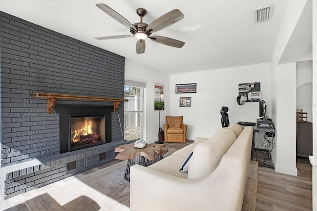 living room featuring hardwood / wood-style flooring, ceiling fan, and a brick fireplace