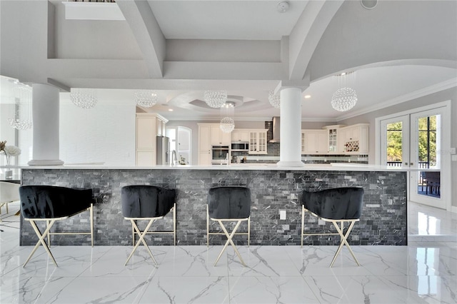 kitchen with decorative light fixtures, decorative columns, ornamental molding, stainless steel appliances, and wall chimney range hood