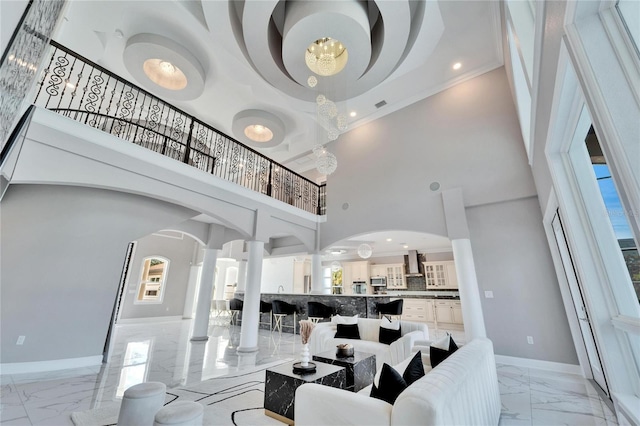 living room featuring a towering ceiling, decorative columns, ornamental molding, a healthy amount of sunlight, and a chandelier