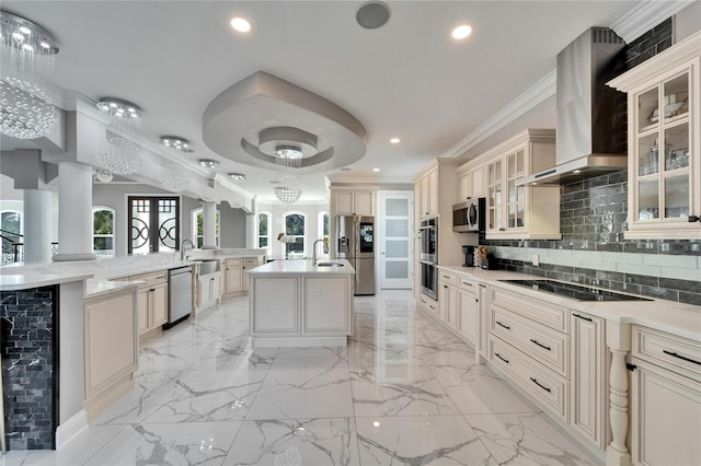 kitchen featuring sink, a kitchen island with sink, stainless steel appliances, cream cabinets, and wall chimney range hood