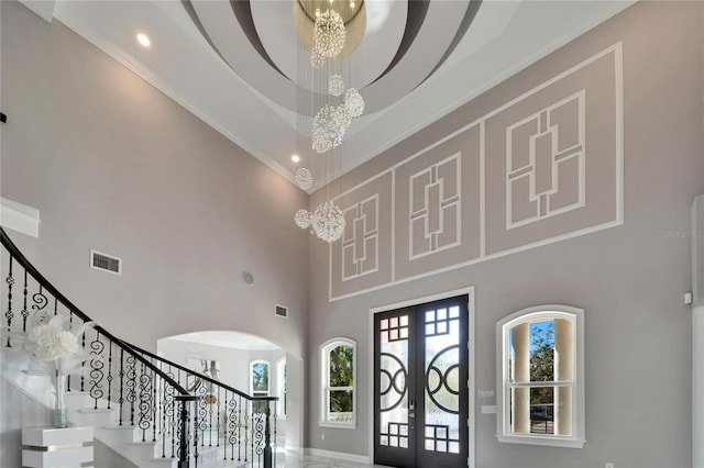 entryway featuring french doors, ornamental molding, a chandelier, and a high ceiling