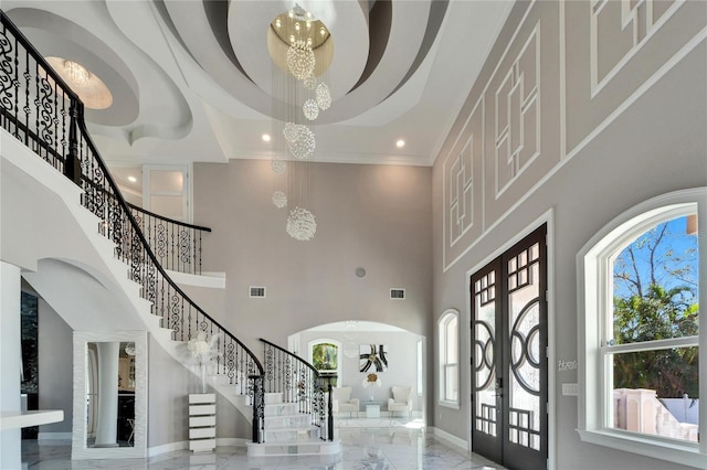 foyer featuring french doors, a towering ceiling, crown molding, and a chandelier