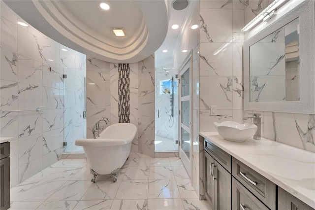 bathroom with tile walls, vanity, independent shower and bath, and a raised ceiling