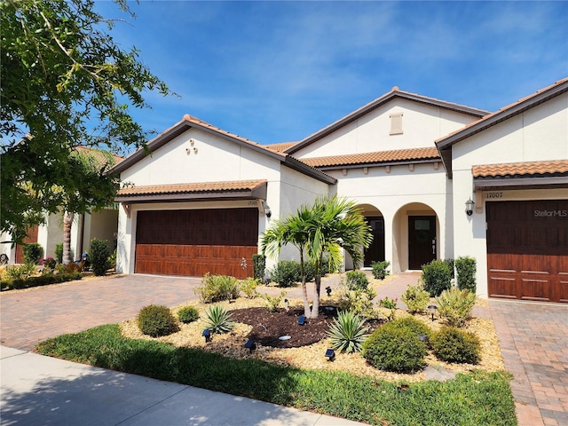 mediterranean / spanish-style house with a tile roof, decorative driveway, a garage, and stucco siding