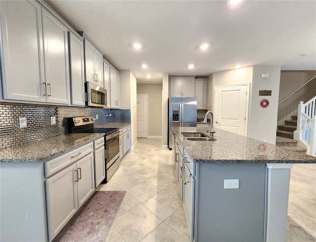 kitchen with sink, gray cabinets, appliances with stainless steel finishes, a kitchen island with sink, and backsplash