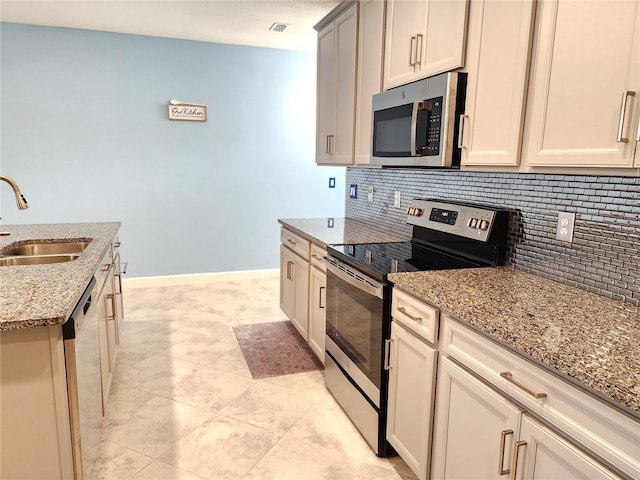 kitchen with sink, appliances with stainless steel finishes, light stone counters, tasteful backsplash, and cream cabinetry