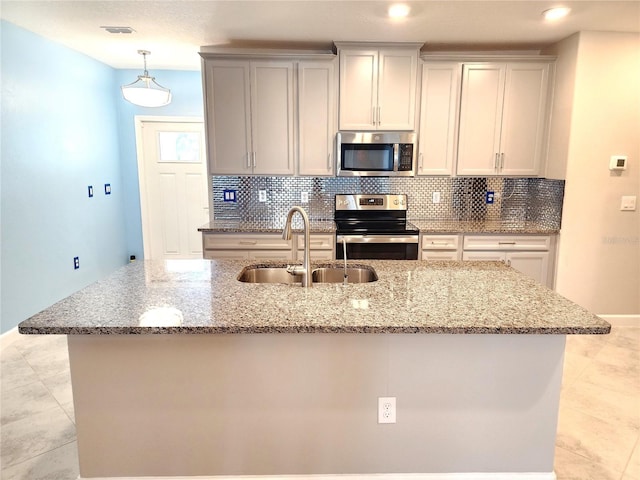 kitchen with an island with sink, appliances with stainless steel finishes, sink, and backsplash