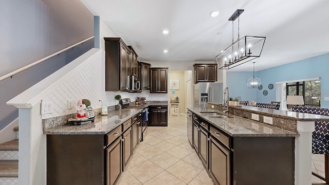 kitchen featuring a breakfast bar, sink, decorative light fixtures, dark stone counters, and stainless steel appliances