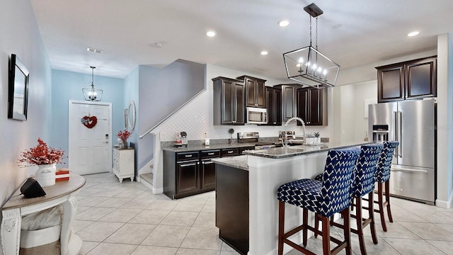 kitchen with stone counters, decorative light fixtures, a kitchen island with sink, dark brown cabinetry, and stainless steel appliances