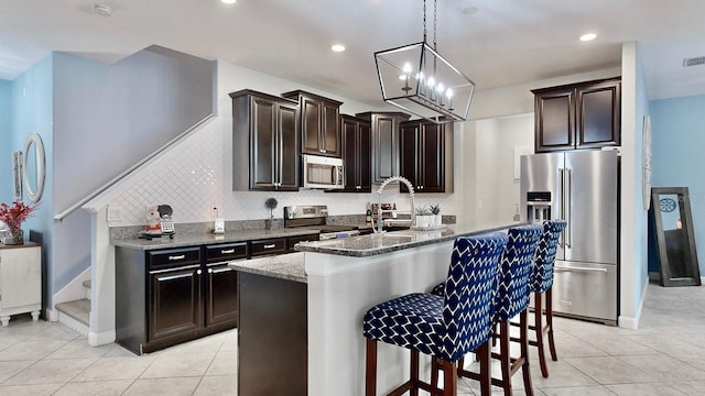 kitchen featuring appliances with stainless steel finishes, a kitchen island with sink, light tile patterned floors, and light stone counters