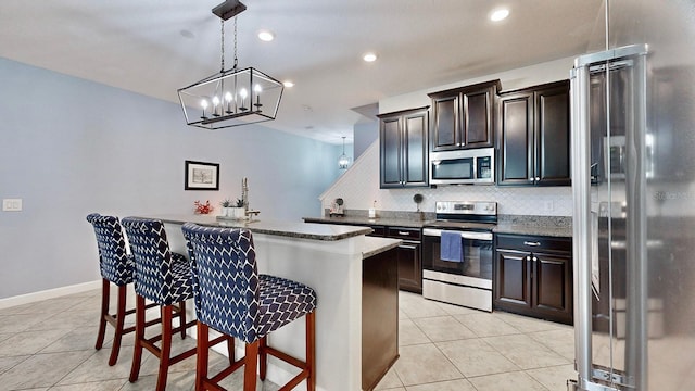 kitchen featuring pendant lighting, a breakfast bar, appliances with stainless steel finishes, a kitchen island with sink, and backsplash