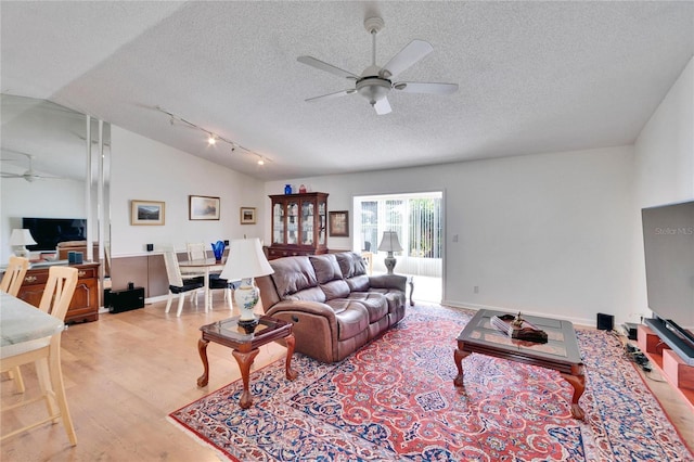 living room with lofted ceiling, light wood-type flooring, a textured ceiling, and ceiling fan