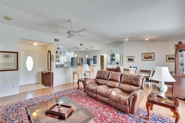 living room featuring lofted ceiling, ceiling fan, light hardwood / wood-style floors, and a textured ceiling