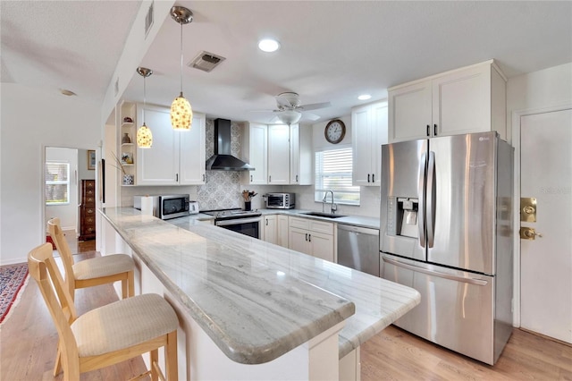 kitchen featuring sink, a breakfast bar, stainless steel appliances, kitchen peninsula, and wall chimney exhaust hood