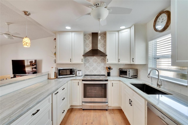 kitchen with appliances with stainless steel finishes, decorative light fixtures, white cabinetry, sink, and wall chimney exhaust hood