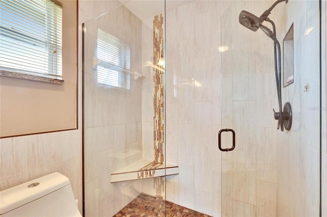 bathroom featuring toilet, a shower with door, and tile walls