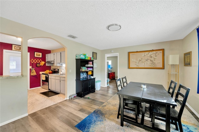 dining room with sink, a textured ceiling, and light hardwood / wood-style flooring