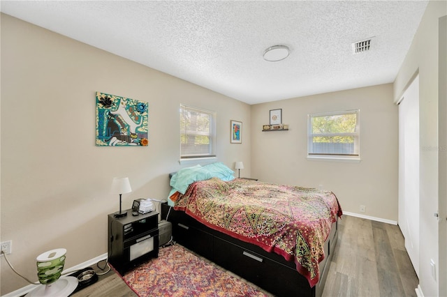 bedroom featuring hardwood / wood-style flooring, multiple windows, and a textured ceiling